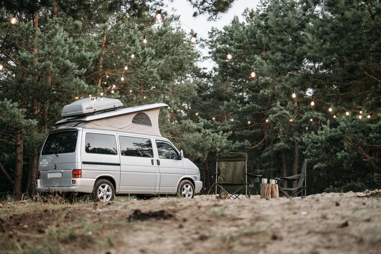 VW Camper mit geöffnetem Aufstelldach auf einem Stellplatz im Wald am Abend